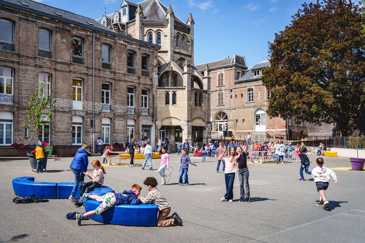 Cour de récréation de l'école avec des élèves en jeu devant les bâtiments anciens