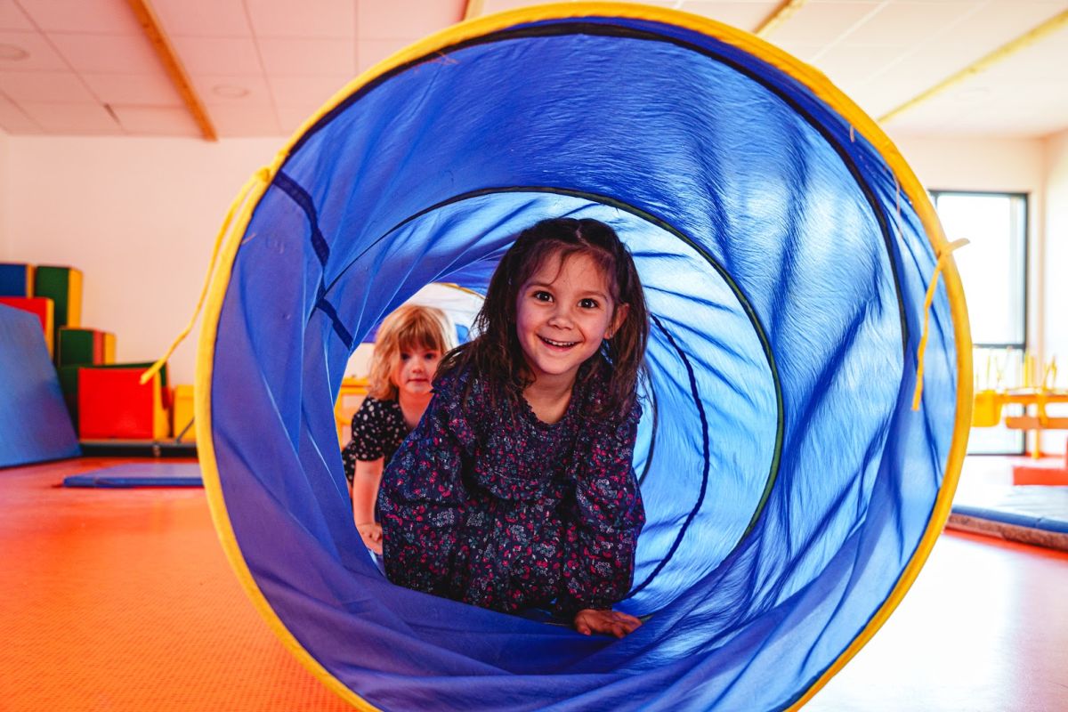 Fillette souriante dans un tunnel de jeu en salle de motricité