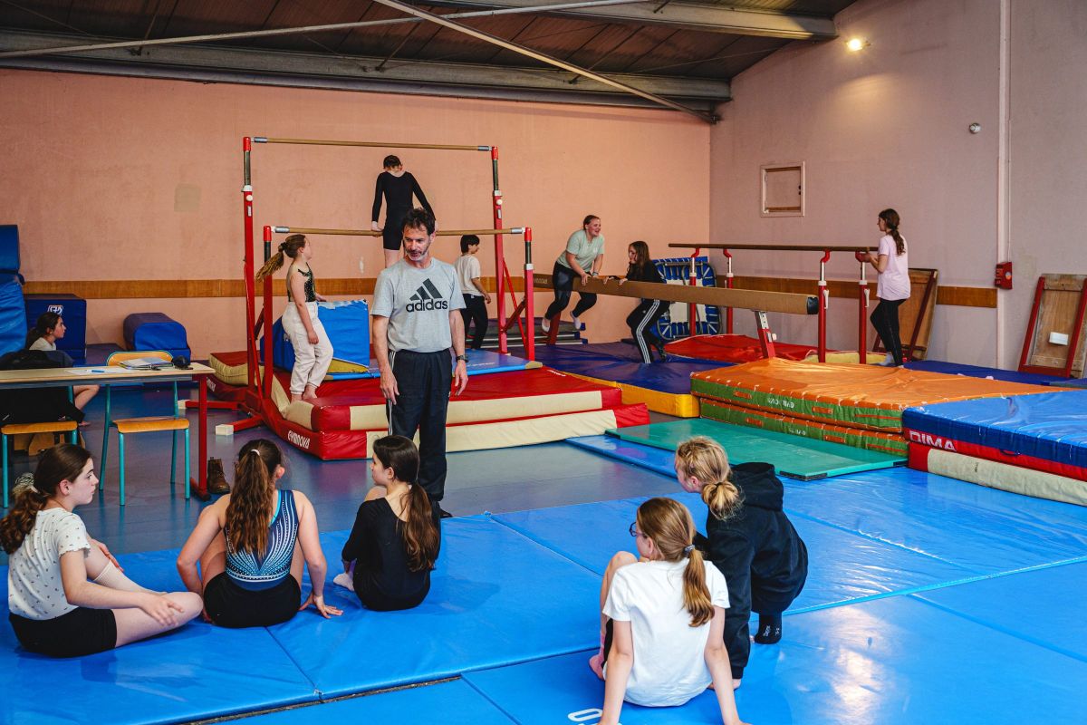 Entraîneur de gymnastique encadrant un groupe de jeunes gymnastes au sol