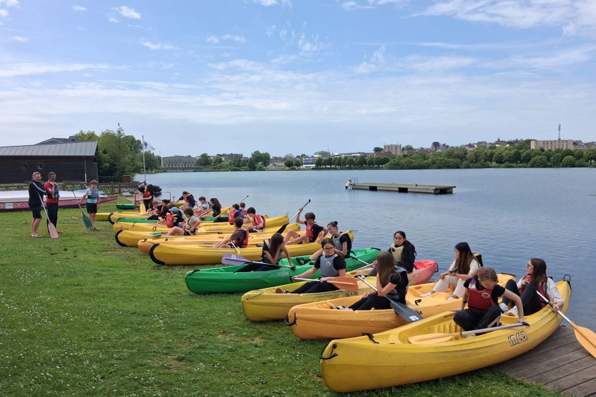 Élèves installés dans des kayaks au bord d'un plan d'eau pour une sortie sportive