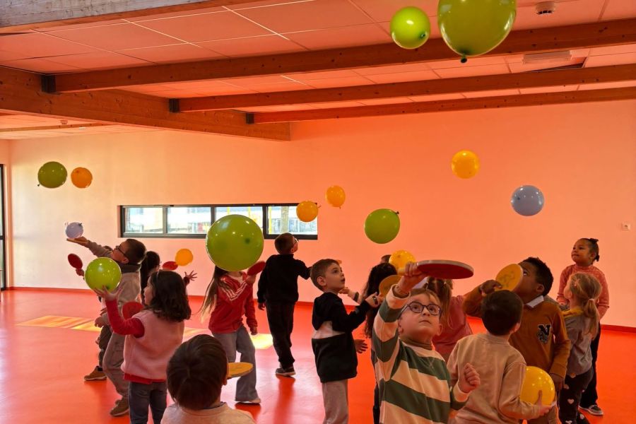 Enfants de maternelle jouant avec des ballons colorés dans une salle d'activités