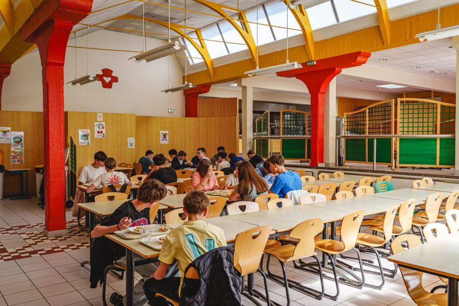 Salle du restaurant scolaire du collège avec ses poutres rouges et jaunes