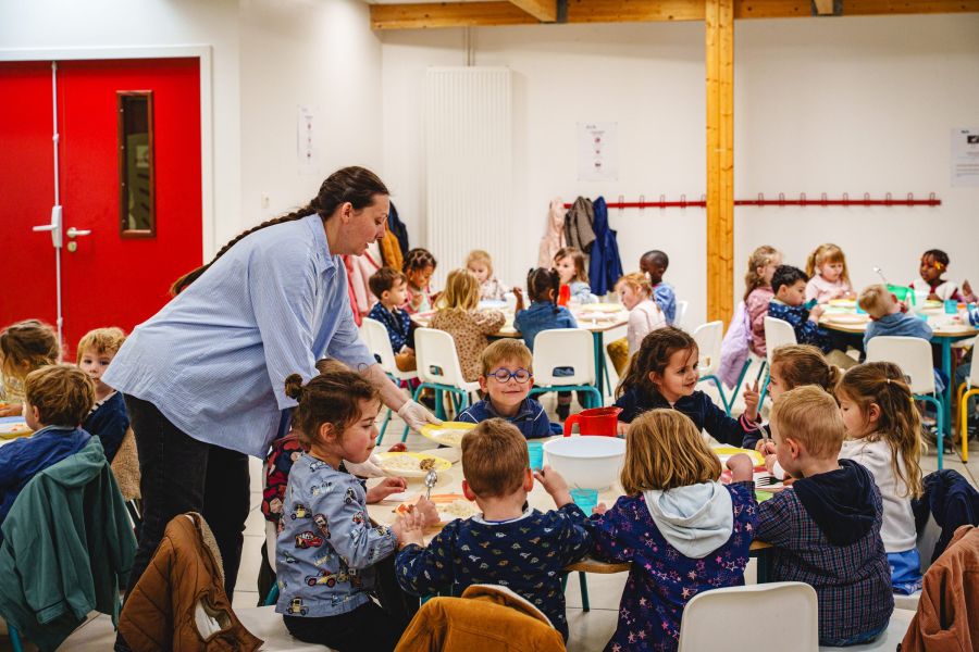 Une adjointe aide de jeunes élèves installés à table au restaurant scolaire