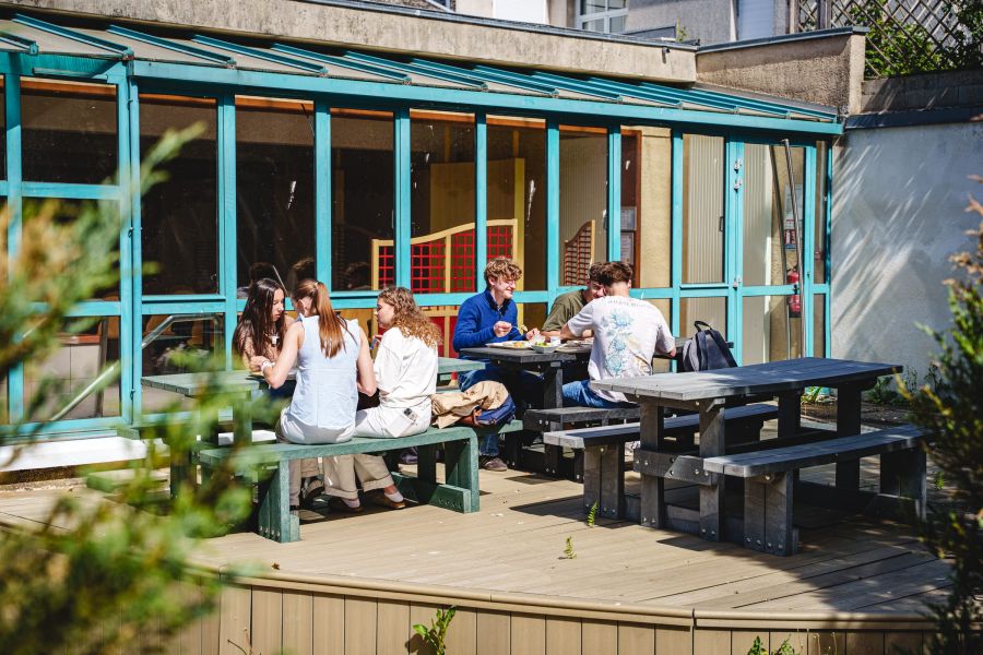 Élèves déjeunant en terrasse ensoleillée près du restaurant scolaire