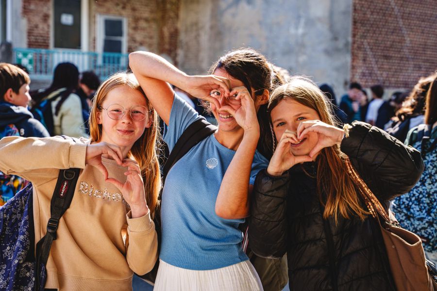 Trois collégiennes complices forment un cœur avec les mains dans la cour