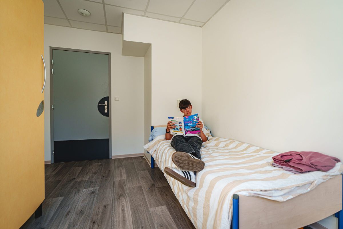Élève installé sur son lit en train de lire dans une chambre de l'internat
