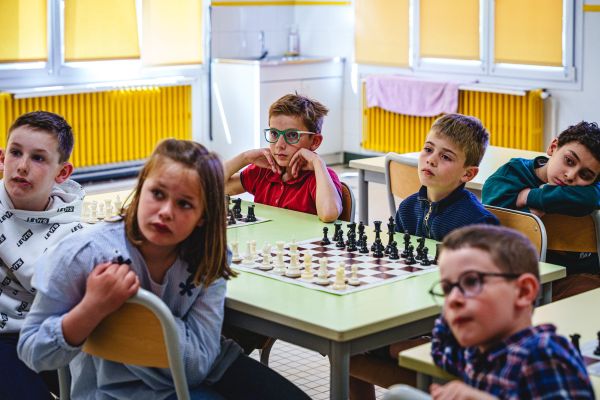 Élèves concentrés autour d'une partie d'échecs pendant un tournoi scolaire