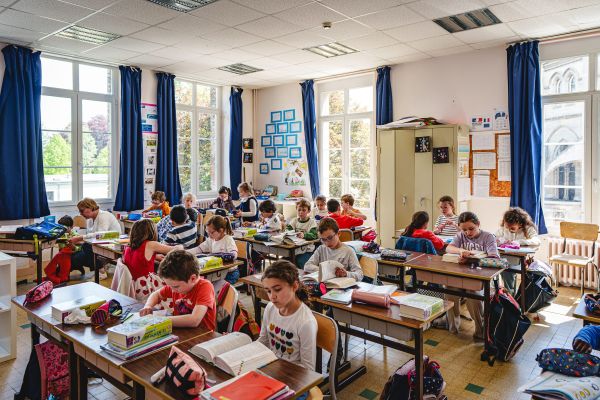 Élèves d'élémentaire en classe, cahiers ouverts sous des rideaux bleus