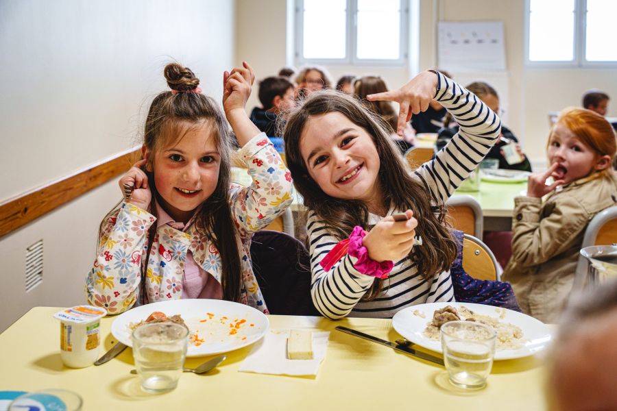 Deux écolières souriantes posent à table pendant le temps du déjeuner