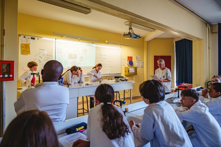Élèves en blouse blanche présentant une expérience scientifique en classe