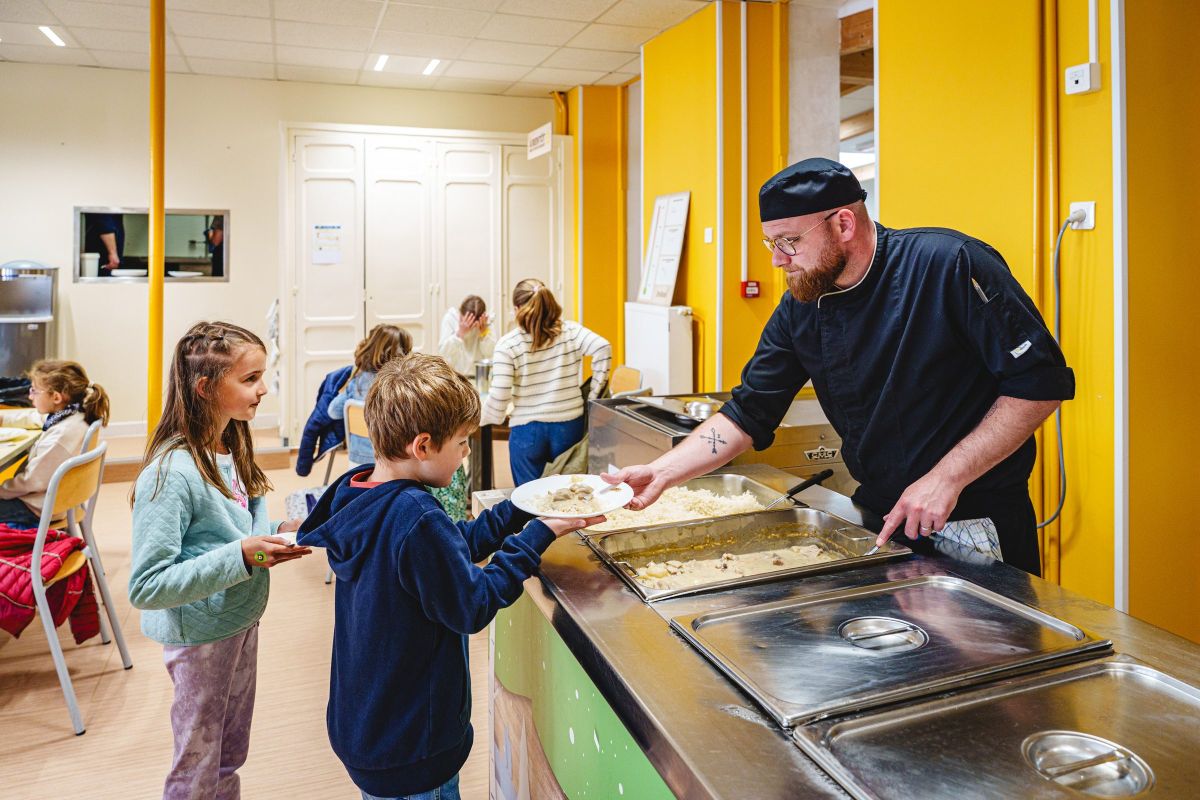 Le cuisinier du restaurant scolaire sert le plat du jour à des élèves