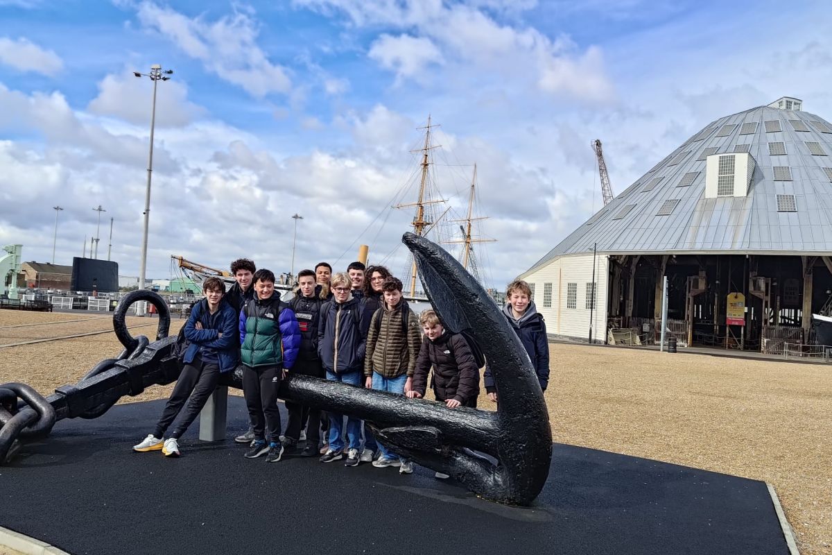Lycéens en voyage scolaire devant une ancre monumentale sur un site maritime