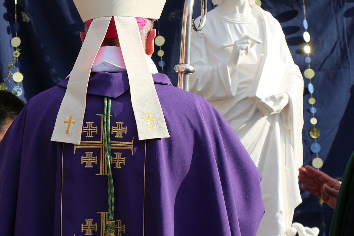 Évêque de dos face à une statue lors d'une célébration religieuse